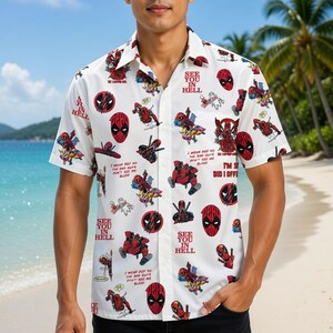Könnte beinhalten: Ein weißes kurzärmeliges Hemd mit Knopfleiste und einem Allover-Druck von Deadpool-Figuren in verschiedenen Action-Posen, roten kreisförmigen Logos sowie dem wiederholten Text "SEE YOU IN HELL" und "I WEAR RED SO THE BAD GUYS DON'T SEE ME BLEED."