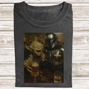 Puede incluir: Camiseta gris oscuro con una imagen humor&iacute;stica de Yoda y The Mandalorian riendo y sosteniendo vasos de cerveza. La imagen est&aacute; ambientada en un bar. Una camiseta divertida con tem&aacute;tica de cultura pop.