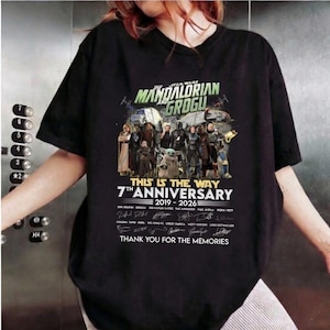 May include: Black t-shirt featuring a graphic of characters from The Mandalorian and Grogu. The design includes the text "The Mandalorian and Grogu", "7th Anniversary 2019-2026", and "This is the Way".