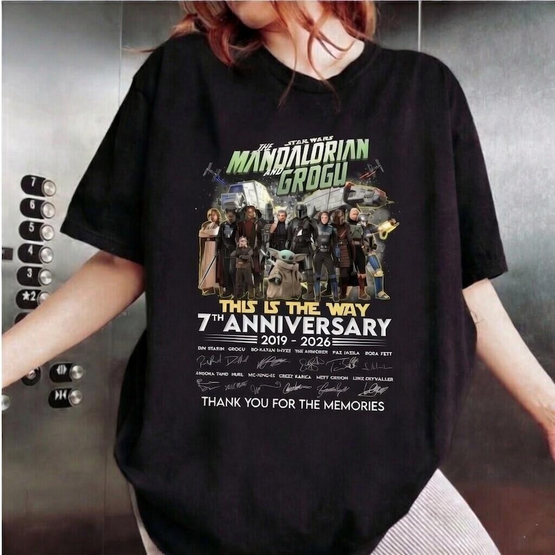 May include: Black t-shirt featuring a graphic of characters from The Mandalorian and Grogu. The design includes the text "The Mandalorian and Grogu", "7th Anniversary 2019-2026", and "This is the Way".