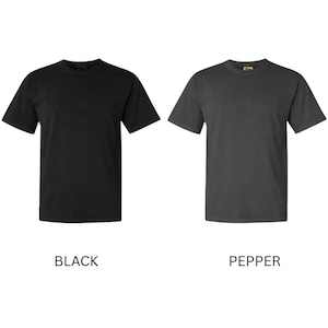 May include: Two short-sleeved t-shirts are shown, one black and one pepper-coloured. The black shirt is on the left, and the pepper-coloured shirt is on the right. The word "BLACK" is below the black shirt, and "PEPPER" is below the pepper-coloured shirt.