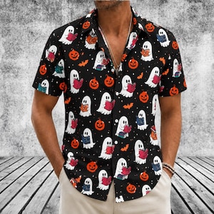 May include: A black short-sleeve button-down shirt featuring a repeating pattern of white ghosts reading colorful books, orange jack-o'-lanterns, and small orange bats. The shirt has a classic collar and a full-length front button closure.