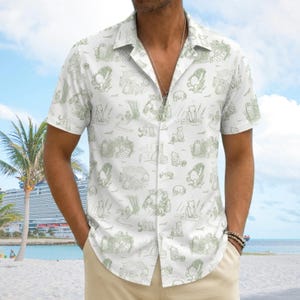 May include: A short-sleeve button-down shirt in white featuring an all-over repeating pattern of light green line-art illustrations depicting various characters in outdoor scenes, including a bear and other small animals in a forest setting.