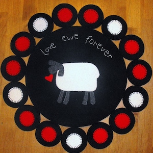 May include: A black felt circle with a white sheep and the text "Love ewe forever" in white embroidery. The circle is surrounded by a ring of 12 smaller circles, alternating red and white.
