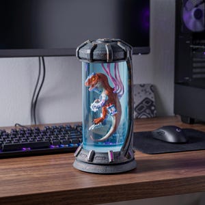 May include: A detailed, futuristic-themed dinosaur figurine encased in a clear, cylindrical container. The orange and brown dinosaur has robotic enhancements and is lit with blue and purple lights. The container sits on a dark, textured base.