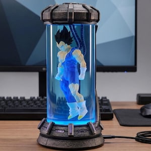 May include: A blue and white figurine of a character from Dragon Ball Z, encased in a cylindrical, glowing blue container. The container has a dark gray base and top, with a USB cable attached. The figurine is in a dynamic pose.
