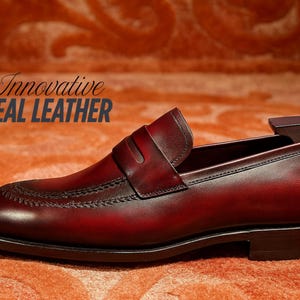 May include: A burgundy leather loafer with a classic design. The shoe features a stitched vamp, a strap across the instep, and a dark sole. The text "Innovative REAL LEATHER" is displayed in the image.
