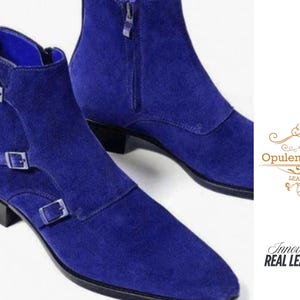 May include: A pair of bright blue suede ankle boots. One boot has two buckle fastenings, while the other has a zip. The boots have a pointed toe and a low heel. The image also includes the text "Opulent Vogue Leather" and "Innovative Real Leather".