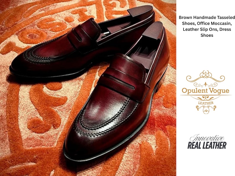 May include: A pair of brown leather slip-on dress shoes with a decorative stitched design. The shoes are displayed on an orange patterned surface. The image includes the text "Brown Handmade Tasseled Shoes, Office Moccasin, Leather Slip Ons, Dress Shoes."