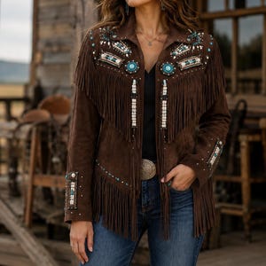 May include: A dark brown suede jacket featuring long fringe detailing across the chest and hem. The jacket is embellished with intricate beadwork and turquoise-colored stones on the shoulders and cuffs, paired with blue denim jeans and a black top.