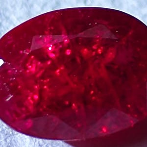 May include: A deep red oval-shaped gemstone with a faceted cut. The gemstone has a high polish and is set in a ring.