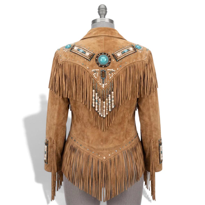 May include: A tan suede jacket featuring long fringe detailing on the back and sleeves. The back is decorated with a central turquoise stone, intricate beadwork, and metallic studs arranged in a V-shaped pattern across the shoulders.