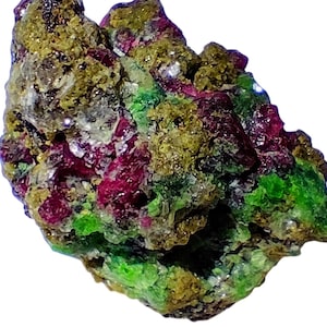 May include: A close-up of a colorful mineral specimen. The rock features a mix of vibrant colors, including deep red, bright green, and golden-brown hues. The texture appears rough and crystalline, with visible facets and formations. The overall shape is irregular.