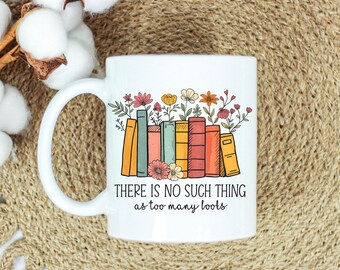 May include: White ceramic mug featuring a colorful illustration of books with flowers on top. The text "THERE IS NO SUCH THING as too many books" is printed below the books. The mug has a curved handle.