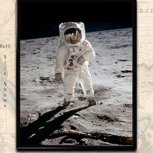 Pode incluir: Uma fotografia a preto e branco de um astronauta de pé na superfície da lua. O astronauta está vestindo um traje espacial branco com um capacete e está olhando para o chão. A sombra do astronauta é projetada na superfície da lua.