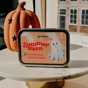 May include: A rectangular tin with the words "Summerween" and a ghost illustration. The tin contains 30 incense cones with a vanilla pumpkin scent. An orange pumpkin with star cutouts is in the background.