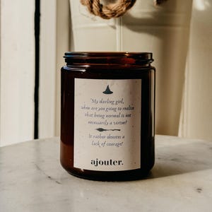 May include: A brown glass candle jar with a white label that reads "My darling girl, when are you going to realise that being normal is not necessarily a virtue? It rather denotes a lack of courage! ajouter."