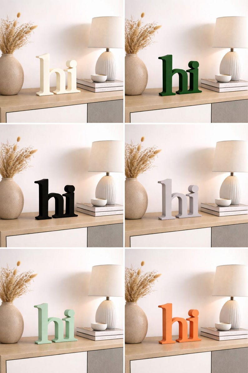 Puede incluir: Una colecci&oacute;n de letreros decorativos de madera con la palabra "hi" en varios colores, incluyendo blanco, verde, negro, gris, verde menta y naranja. Los letreros se exhiben sobre una superficie de madera clara, junto a jarrones, l&aacute;mparas y libros.