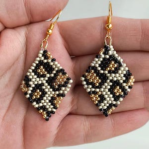 Op de afbeelding: Een paar zwarte, witte en gouden kralen oorbellen met een diamantvorm. De oorbellen zijn gemaakt met behulp van een brick stitch techniek. De afbeelding bevat de tekst "BRICK STITCH EARRINGS" en "PDF PATTERN".
