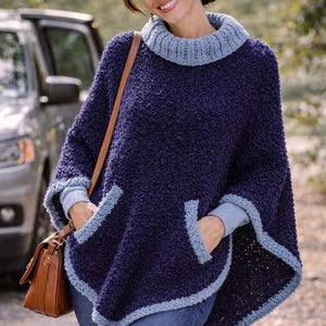 May include: A dark navy blue textured poncho with a light blue ribbed turtleneck collar and matching light blue trim along the hem and pocket openings. The text MOODY BLUES is printed in white in the upper left corner of the image.