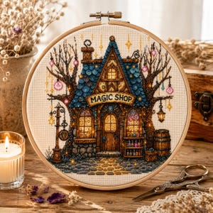 May include: A cross-stitch embroidery in a wooden hoop depicting a house labeled MAGIC SHOP with a blue roof, stone walls, and glowing windows. The scene includes two large trees with hanging lanterns, a wooden barrel, and small potion bottles.