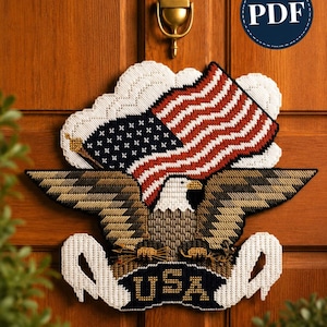 May include: A plastic canvas needlepoint wall hanging featuring a bald eagle with outstretched wings, clutching arrows and an olive branch. Above the eagle is a waving American flag. A banner at the bottom displays the text USA in gold letters.