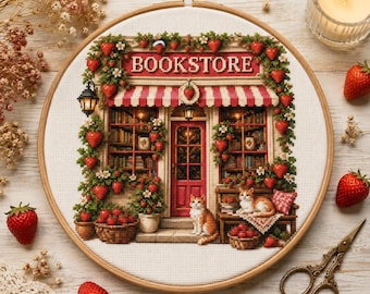 以下が含まれることがあります： 書店を描いたクロスステッチ刺繍の円形刺繍枠。赤と白のストライプのオーニング、本でいっぱいの棚、2匹の猫、イチゴのつるがデザインされています。BOOKSTOREという文字が赤色で刺繍されています。