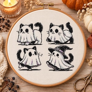 Può includere: Un telaio da ricamo circolare in legno contenente un pannello di tessuto bianco con quattro figure di gatti ricamate a punto croce. Ogni gatto indossa un costume da fantasma bianco, e uno indossa anche un cappello da strega nero con dettagli.