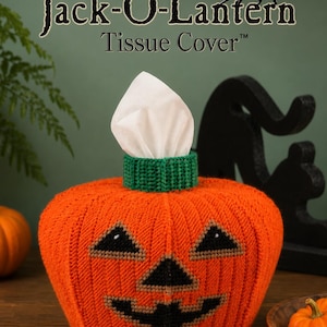 May include: An orange knitted Jack-O-Lantern tissue cover with a green top collar. The pumpkin features a black stitched face with triangular eyes, a triangular nose, and a wide jagged mouth. A white tissue protrudes from the center opening.