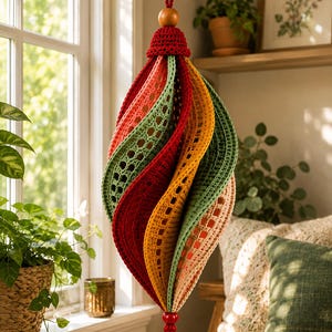 May include: A hanging crochet ornament featuring a spiraling, teardrop-shaped design with alternating panels of red, mustard yellow, sage green, and light peach yarn. The piece is topped with a wooden bead and finished with a small red bead at the base.