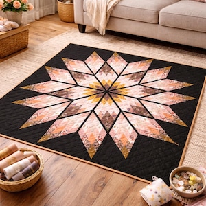 May include: A square quilt featuring a large central star pattern composed of diamond-shaped segments in shades of pink, peach, and gold. The star is set against a solid black background with a diamond-stitched texture and a thin tan border.