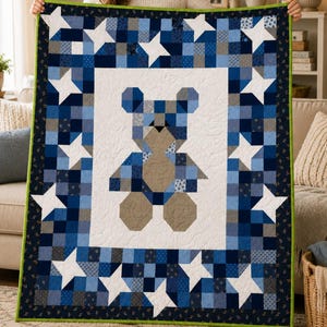 May include: A rectangular quilt featuring a central teddy bear motif composed of blue, grey, and tan fabric squares on a white background. The border consists of a blue and grey patchwork pattern with white star shapes and a bright green edge.