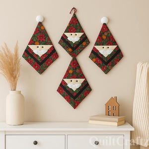 May include: Four Christmas-themed wall hangings shaped like Santa Claus hats. The hats feature a red floral pattern with black stripes and a white beard. Each is hung with a white knob or red string. A vase with dried plants and a small house decoration are on a white dresser.