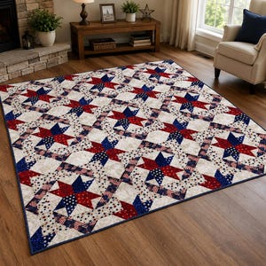 May include: A rectangular quilt featuring a repeating star pattern in red, white, and blue. The design incorporates fabric prints of American flags and small stars on a cream-coloured background, finished with a dark blue border trim.