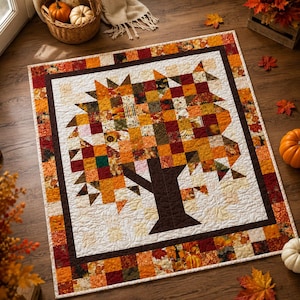 May include: A square quilt featuring a central tree motif constructed from small fabric squares in shades of orange, red, yellow, and brown. The tree is set against a white background with a quilted leaf pattern and a multi-colored patchwork border.