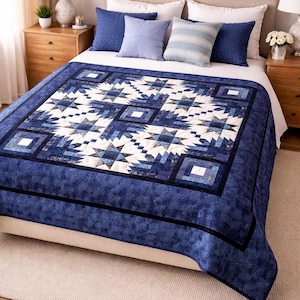 May include: A blue and white quilt with a geometric star pattern is displayed on a bed. The quilt features a dark blue border and a central design of white and various shades of blue. Several blue pillows complete the bedding ensemble.
