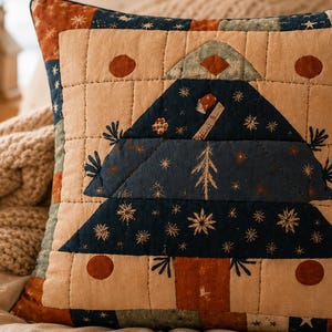 May include: A square quilted throw pillow featuring a central dark blue Christmas tree appliqué on a cream background. The design includes small star patterns, rust-colored circles, and a grid-stitched texture. The border consists of patchwork squares in shades of blue, rust, and cream with star motifs.