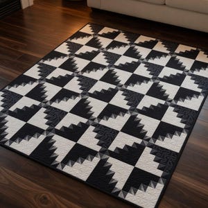May include: A rectangular area rug with a geometric pattern in black and white. The design features alternating squares with a repeating triangular motif. The rug is placed on a dark wood floor, with a sofa visible in the background.