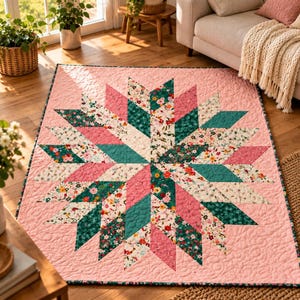 May include: A rectangular quilt featuring a central starburst pattern composed of diamond-shaped fabric patches. The design incorporates solid pink, dark teal, and floral-patterned fabrics with white, pink, and green blossoms on a light background.