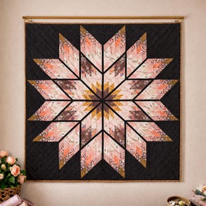 Könnte beinhalten: Eine große, quadratische Steppdecke mit einem Sternmuster. Der Stern besteht aus verschiedenen gemusterten Stoffen in Rosa-, Pfirsich- und Brauntönen, vor einem schwarzen Hintergrund. Die Steppdecke hängt an einer Holzstange.