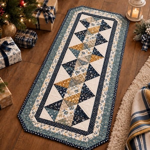 May include: A rectangular quilted table runner featuring a geometric pattern of triangles in shades of navy blue, mustard yellow, and cream. The runner is bordered by multiple fabric strips with floral and polka dot prints in blue and white tones.