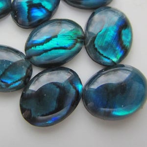 May include: Oval-shaped iridescent cabochons in shades of teal, turquoise, and deep blue. The polished stones have a glossy finish, reflecting light with a shimmering, opalescent effect. These decorative stones are ideal for jewelry making.