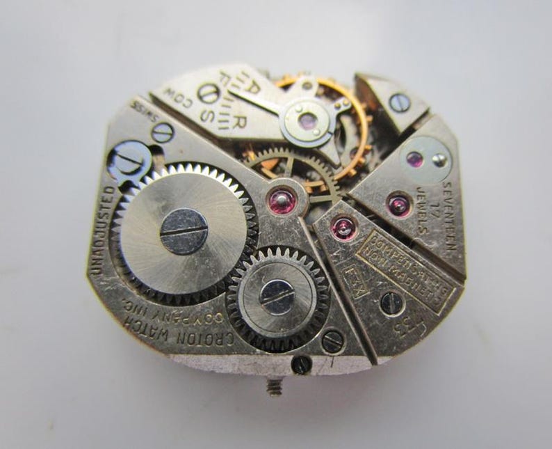 May include: A detailed view of a vintage Croton watch movement. The silver mechanism displays intricate gears, jewels, and the text "SEVENTEEN JEWELS". The watch movement is marked "UNADJUSTED" and "SWISS".