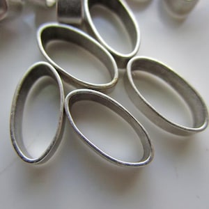 May include: Close-up of several small, oval-shaped, silver-colored metal rings. The rings are arranged on a white surface, with some overlapping. The rings have a smooth, polished appearance.