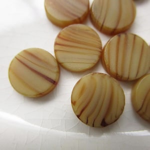 May include: A collection of round, flat beads with a light tan base color and brown, swirled stripe patterns. The beads are arranged on a white surface, showcasing their unique, naturalistic design. These beads are ideal for jewelry making.