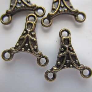 Peut inclure: Plusieurs connecteurs métalliques de couleur bronze antique. Chaque connecteur a une forme triangulaire avec trois trous circulaires et des détails décoratifs. Les connecteurs sont probablement destinés à la fabrication de bijoux ou à d'autres projets d'artisanat.