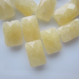 May include: A collection of faceted, rectangular beads in a pale yellow hue. The beads have a geometric, cut design, catching the light. These gemstone beads are ideal for jewelry making, such as necklaces and bracelets.
