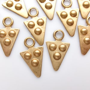May include: Gold-colored metal triangle charms with three raised circular studs and a loop at the top. The charms are arranged on a white surface, suitable for jewelry making or craft projects.