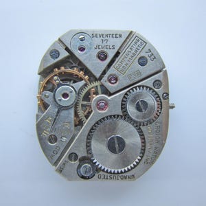 May include: Detailed view of a watch mechanism, showcasing intricate gears, jewels, and inscriptions. Text includes "SEVENTEEN 17 JEWELS", "COMPENSATING NON MAGNETIC", and "CROION WATCH COMPANY INC". The movement is silver with gold gears.