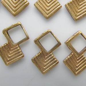 May include: Gold-toned metal jewellery findings with a geometric design. The findings are shaped like a square with a smaller square cut out in the centre. The larger square has a chevron pattern.